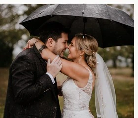 Bride and groom kissing beneath an umbrella on a rainy wedding day