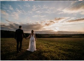 Bride and groom walking across a field at sunset